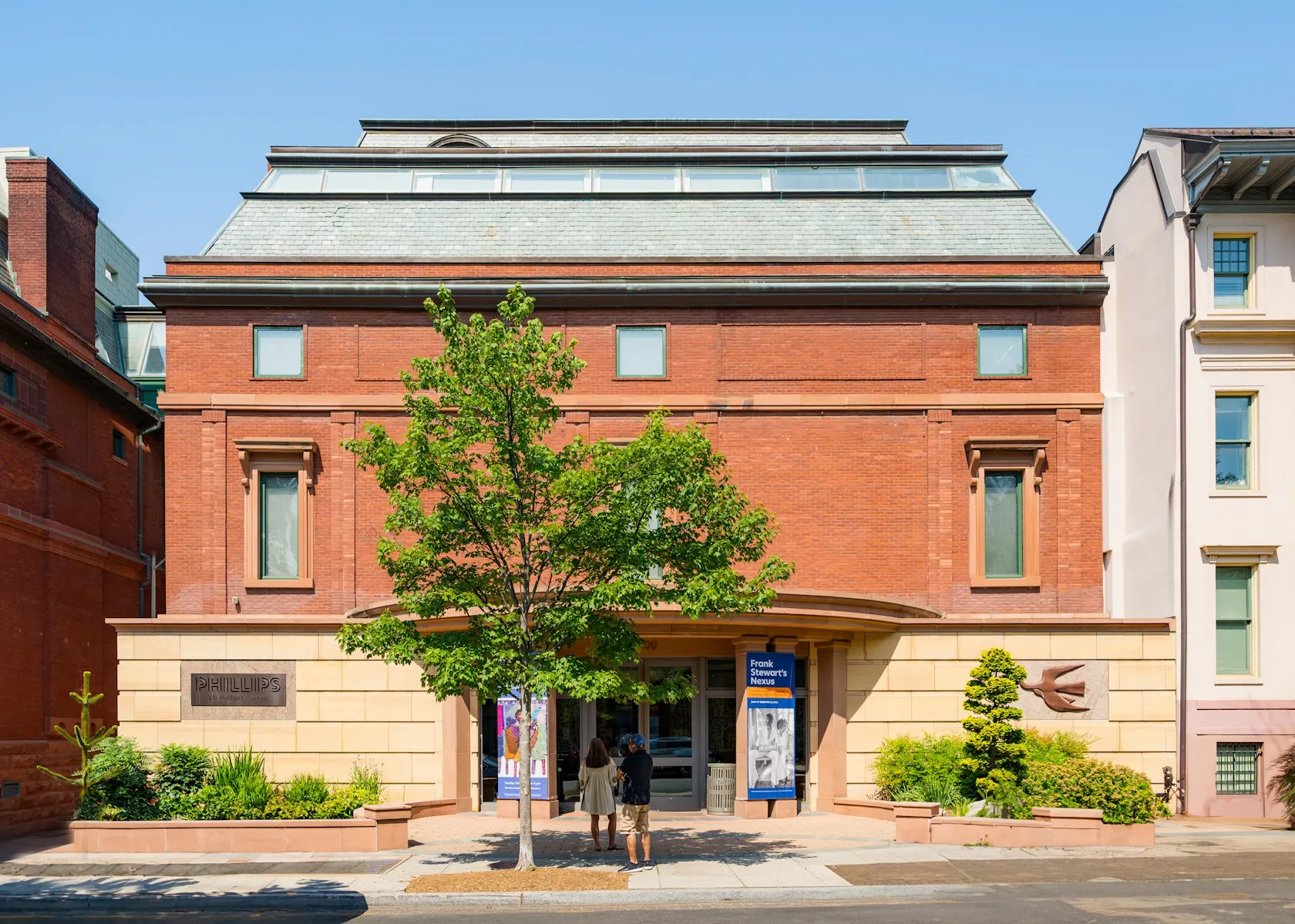 The Phillips Collection, a red-brick building with blue awnings and a street tree on a sunny day