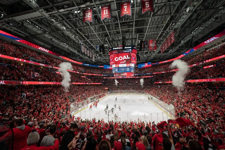 Hockey arena packed with fans in red as goal appears on scoreboard, smoke jets