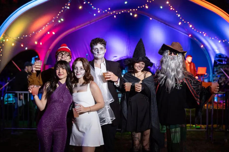 Group in Halloween costumes poses on a lit stage with glowing arches