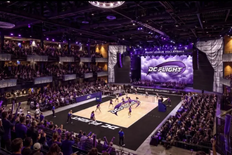 Packed indoor arena with purple lighting, performers on court and large video screen