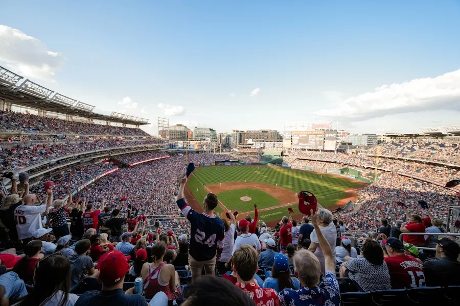 Packed baseball stadium crowd watching game from upper deck, green field below