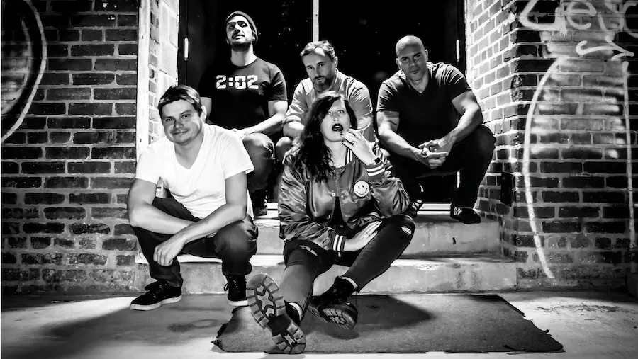 Black-and-white group pose in brick alley, three crouching in front, one seated behind