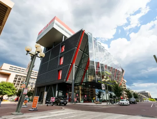 El exterior moderno del Museo Internacional del Espionaje en Washington, DC, presenta un diseño llamativo con detalles en rojo y paneles de vidrio bajo un cielo nublado.