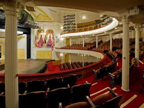 The historic Ford's Theatre features elegant red seating, curved balconies, and a stage framed by rich gold accents.