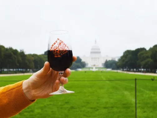 Une main lève un verre de vin rouge sur le National Mall avec le Capitole des États-Unis en arrière-plan.