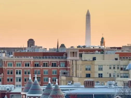 A photo of the DC skyline at sunset with the Washington Monument just beyond the historic buildings below. 