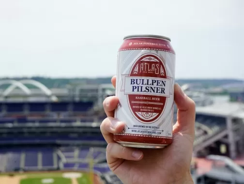 A hand holds a beer can with a view of Nationals Park in the background. 