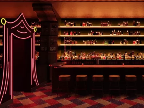 A dimly lit, retro-style bar with a backlit liquor display, a row of wooden stools and a neon pink curtain-shaped entrance on the left.
