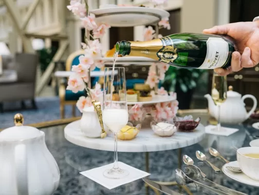 A hand pours champagne into a glass on a table set for a lavish high tea. 