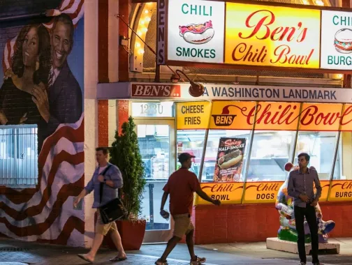 People walk by Ben's Chili Bowl at night.