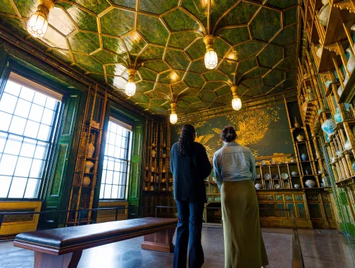 Two people view the ornate green-and-gold Peacock Room filled with ceramics at a museum in Washington, DC
