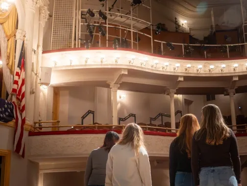 A group of people stand on stage, looking up into the box seating section of the historic Ford's Theatre.