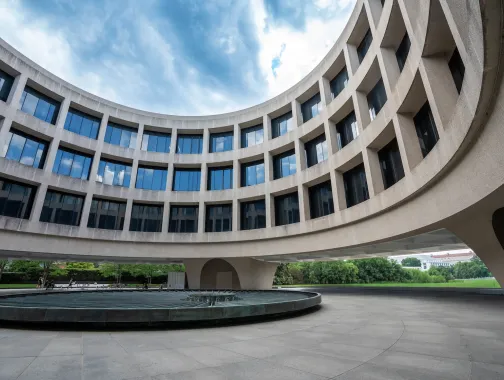 Curved modern building with large windows surrounding a circular fountain under blue sky