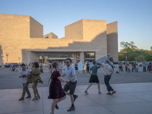 People walking in a plaza outside a modern beige stone building at dusk