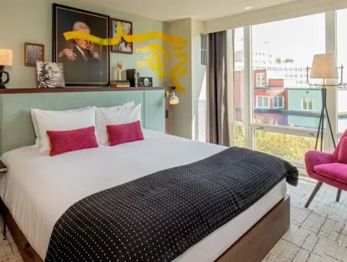 Photo of bright bedroom with king bed, pink pillows and chair, balcony view through large windows