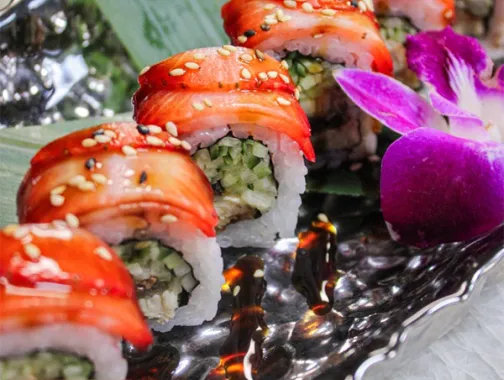Sushi rolls drizzled with sauce on a black platter with a purple orchid