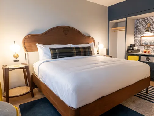 A modern hotel room with king bed, blue-gray walls and open closet nook