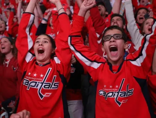 Crowd in red Washington Capitals jerseys cheering with arms raised