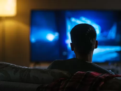 boy facing the television watching it in the dark