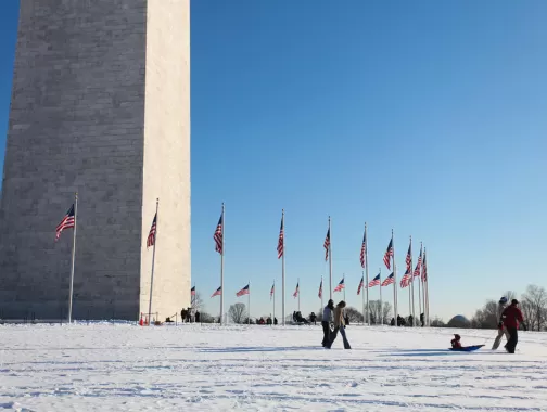 Family on snowy Washington Monument grounds on the National Mall - The best snow day activities in Washington, DC