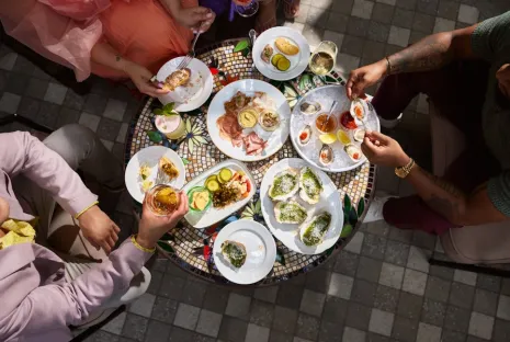 A group shares a meal of oysters, charcuterie and cocktails at an outdoor table.