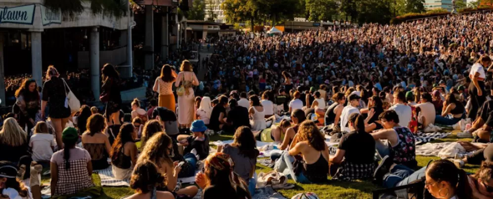 concertgoers seated on the lawn in front of a pavilion