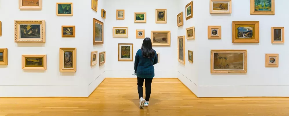 Um visitante explora uma galeria na The Phillips Collection, onde pequenas pinturas emolduradas em vários estilos são dispostas em paredes brancas, criando uma experiência artística envolvente.
