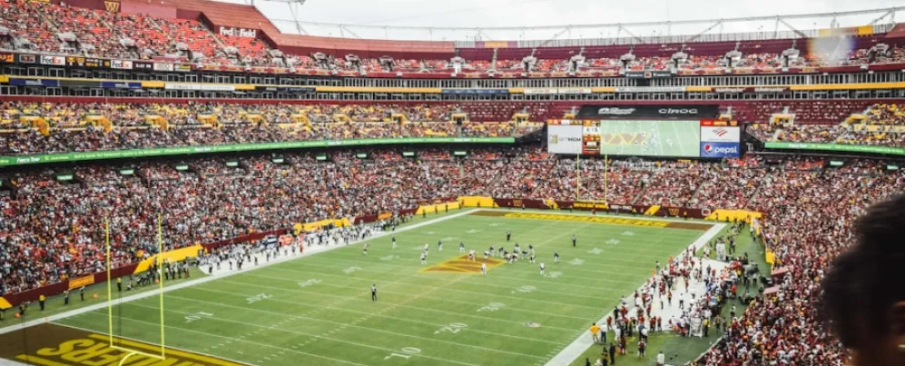 A packed stadium during a Washington Commanders football game, with fans filling the stands and players on the field at FedExField.