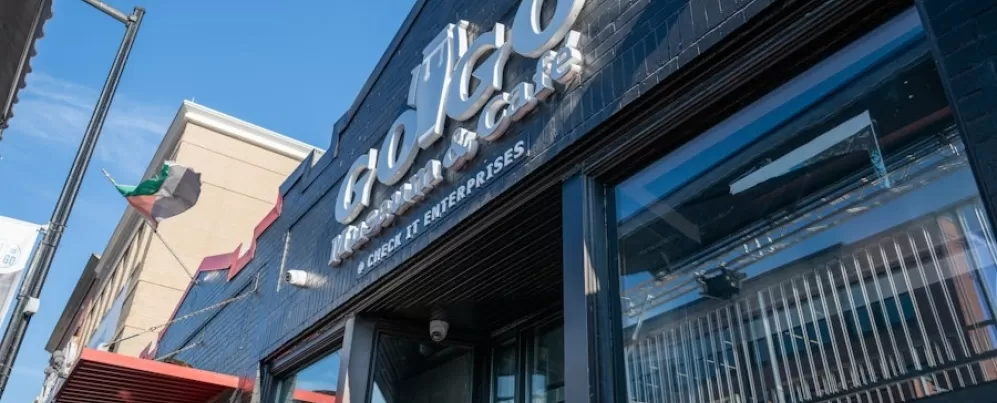 A entrada do Go-Go Museum & Café apresenta uma sinalização ousada em um prédio de tijolos pintados de preto sob um céu azul brilhante.