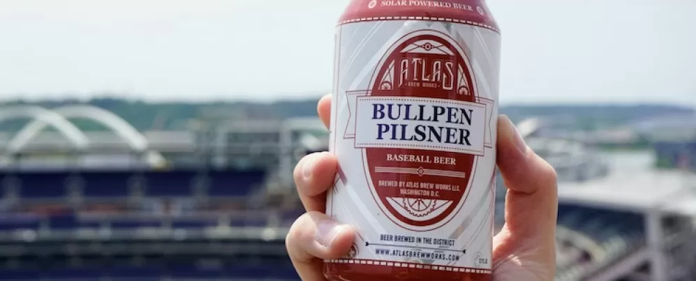 Una mano sostiene una lata de cerveza con una vista del Nationals Park en el fondo.