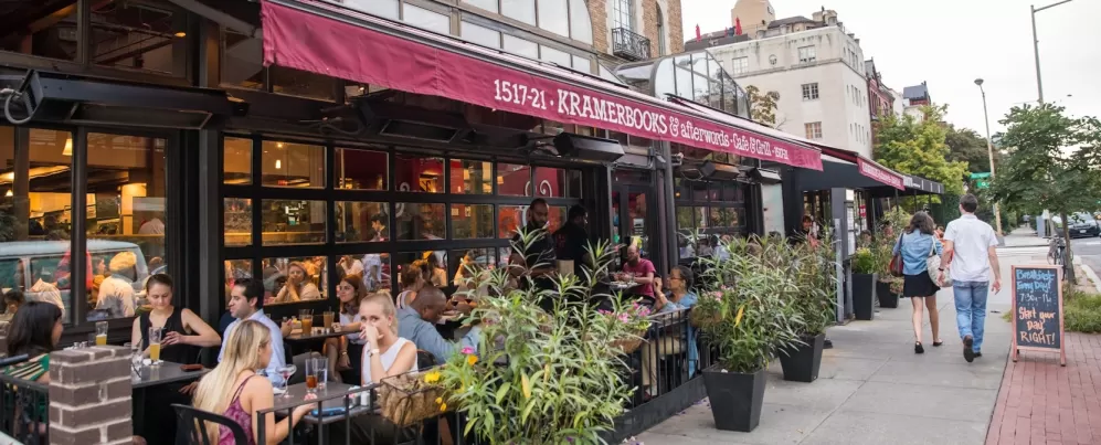 Diners enjoy outdoor seating at Kramerbooks & Afterwords Café in Dupont Circle as pedestrians stroll past the bustling sidewalk café.