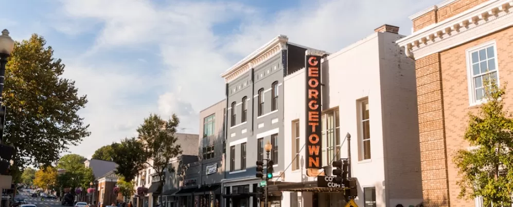 Voetgangers en auto's lopen langs winkels onder een felgekleurd Georgetown-bord in een drukke straat in de historische wijk Georgetown in Washington, D.C.