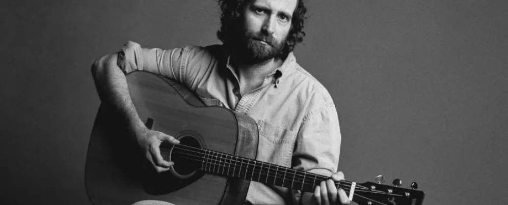 Nghệ sĩ hài kiêm nhạc sĩ Kyle Mooney tạo dáng với cây đàn guitar acoustic trong bức ảnh quảng cáo đen trắng.
