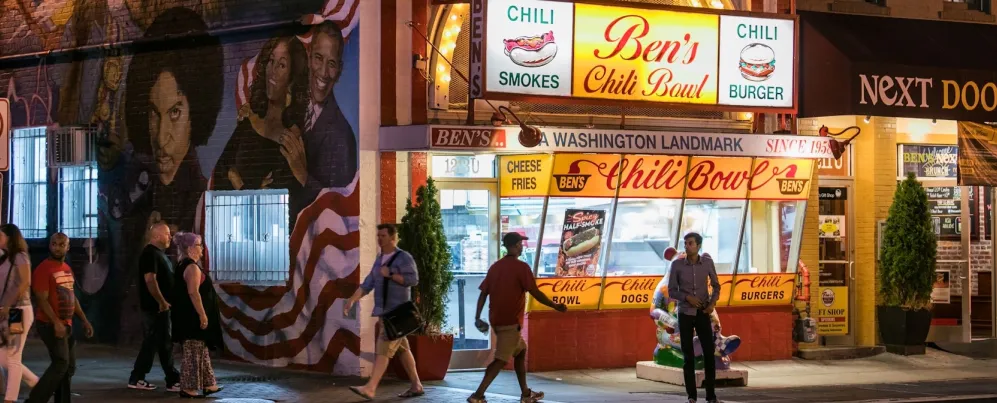People walk by Ben's Chili Bowl at night.