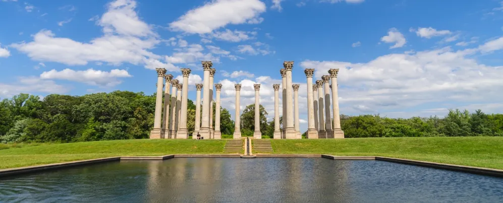 Die Säulen des National Capitol ragen hoch auf einem grasbewachsenen Hügel empor und spiegeln sich unter einem strahlend blauen Himmel in einem Teich im US National Arboretum.