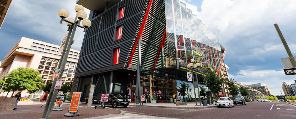 The modern glass and steel exterior of the International Spy Museum in Washington, DC, featuring red architectural accents and pedestrians along the street.