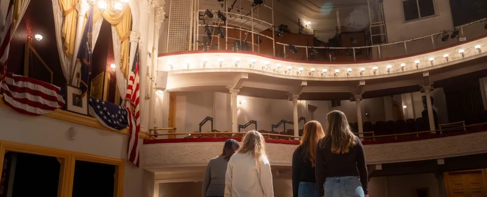 A group of people stand on stage, looking up into the box seating section of the historic Ford's Theatre.