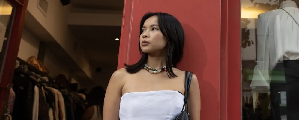 Woman in strapless white top standing by red doorway, looking left