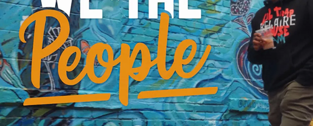 Chef Anthony Jones standing by mural, alongside “We The People” graphic