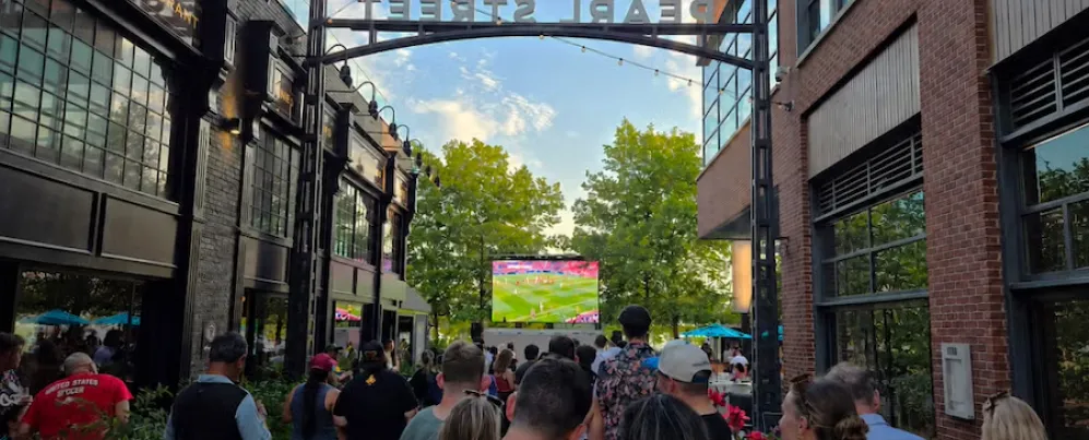 Foule regardant un match de football sur un écran dans une rue piétonne de la ville