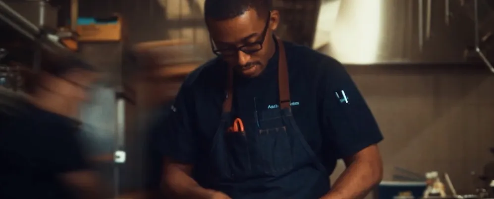 Chef in a dim kitchen preparing food under warm task lighting