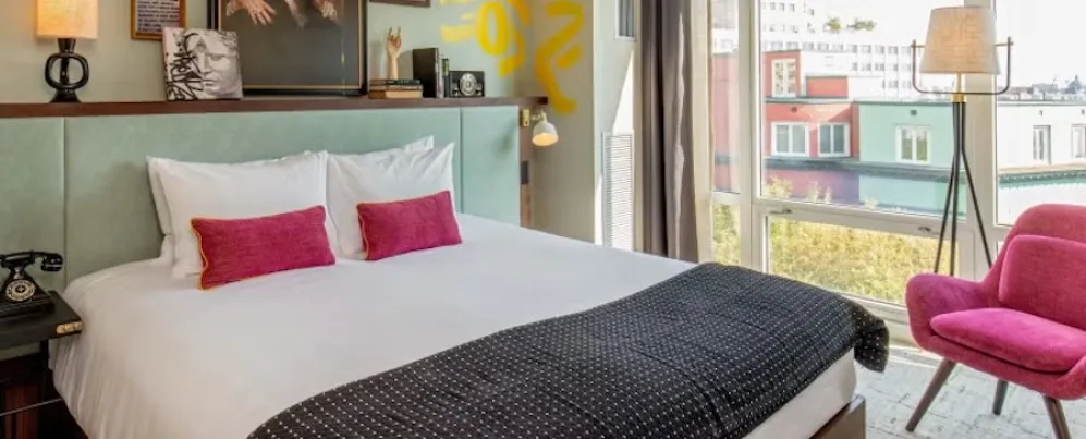 Foto eines hellen Schlafzimmers mit Kingsize-Bett, rosa Kissen und Sessel, Balkonblick durch große Fenster