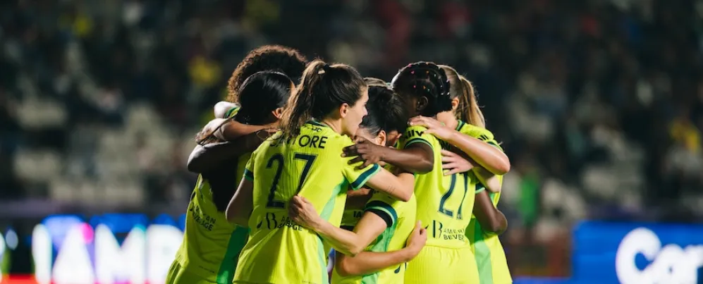 Um grupo de jogadores de futebol com camisas verde-neon se reúne no campo de um estádio.