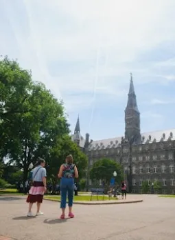 Two people walk along a tree-lined path toward the Georgetown University in Washington, DC.