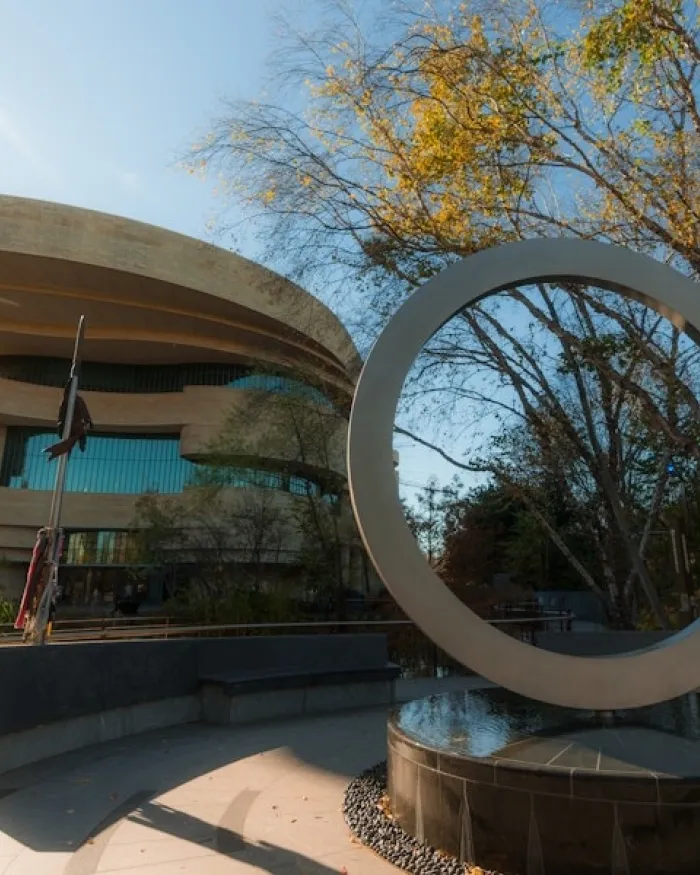 Circular sculpture in front of the National Museum of the American Indian surrounded by trees.