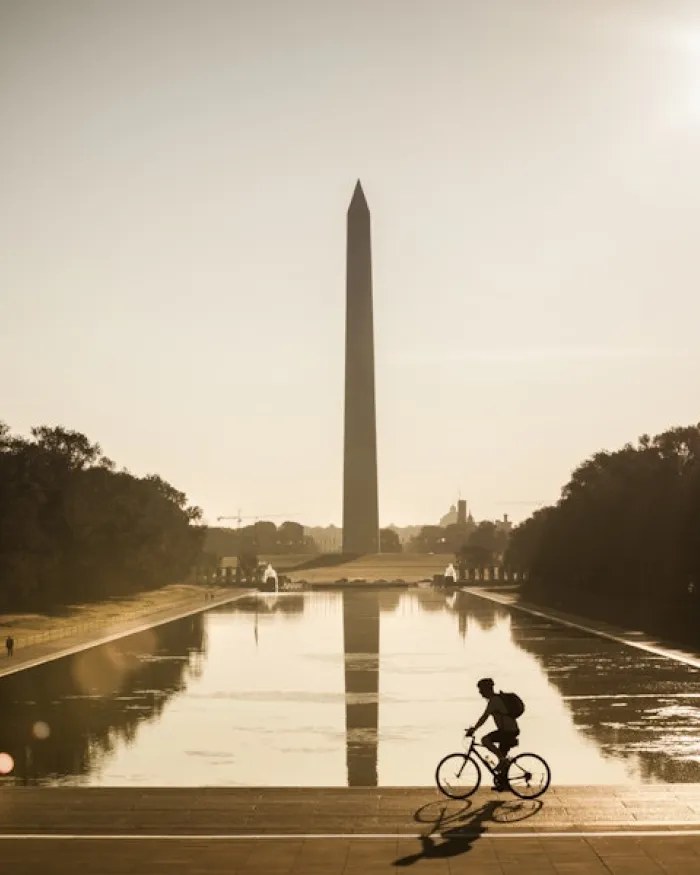 A cyclist rides past the Reflecting Pool with the Washington Monument rising in the background at sunrise.