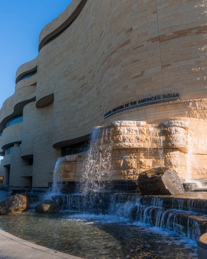 The National Museum of the American Indian’s curved stone exterior and cascading fountain glow in the sunlight on the National Mall in Washington, DC.