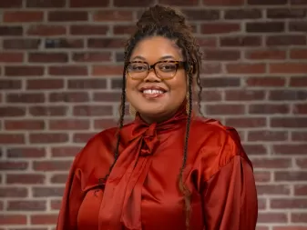 Uma mulher de blusa vermelha e óculos sorri para uma foto profissional. 