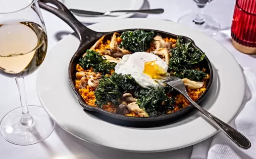 skillet with paella, kale and fresh egg on a white table spread

